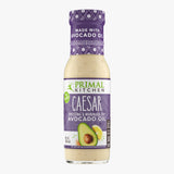 A bottle of no-dairy Primal Kitchen Caesar Dressing & Marinade made with avocado oil and cage-free eggs, with a purple label, on a light grey background. 