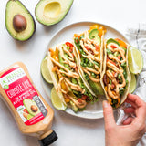 Three veggie flour tacos drizzled with chipotle lime mayo on a white plate with cut up limes next to a cut avocado and a squeeze bottle of Primal Kitchen Chipotle Lime Mayo.