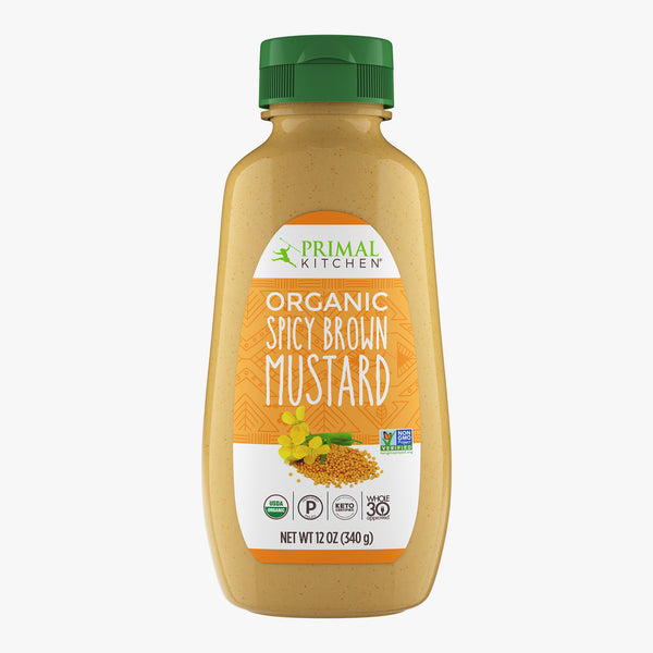 A bottle of Primal Kitchen Organic Spicy Brown Mustard with an orange label and green lid on a light grey background.