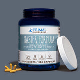 A uncapped blue bottle of Primal Blueprint Master Formula with a blue and white label next to a white cap and yellow supplements on a light grey background.